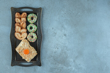 Dessert arrangement with flaky cookies, a cake slice, donut and on an ornate tray on marble background