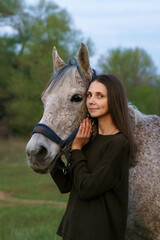 Girl hugging a fleabitten grey horse and looking at the camera
