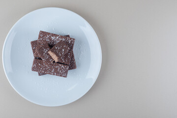 Chocolate coated wafers stacked on a white platter on marble background