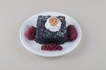 Chocolate cake and red pine cones on a platter on marble background