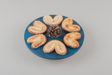 Pine cone surrounded by flaky cookies on a platter on marble background