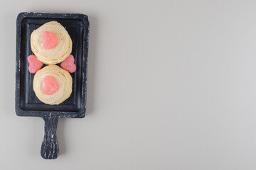 Flaky cakes and heart marmelades on a black tray on marble background