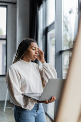 Fototapeta premium Focused african american businesswoman in sweatshirt holding laptop in office.