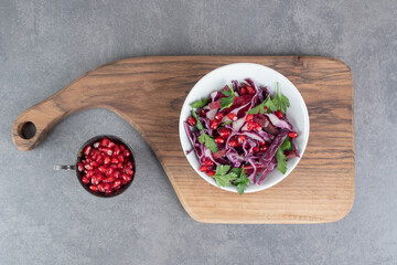 Bowl of vegetable salad on wooden board with pomegranate seeds