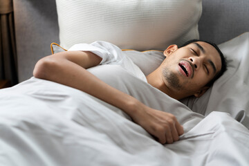 A young bearded man sleeps with his mouth open and makes a loud snore lying down on bed, tired and deep sleep. Making noise and annoying his partner.