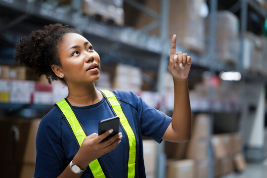 Young African American warehouse worker counting shipment on shelves align with online total box number in stock on smartphone to confirm the inventory before delivery. Logistic business.
