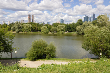 Fototapeta na wymiar Pond, park with trees and bushes, embankments with vacationers, skyscrapers. Moscow, summer day, cloudy sky.