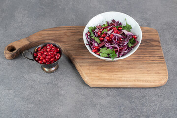 Bowl of vegetable salad on wooden board with pomegranate seeds