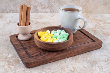 Cup of tea, cinnamon and candies on wooden board
