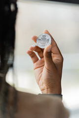 KYIV, UKRAINE - APRIL 27, 2022: Blurred african american businesswoman holding silver bitcoin in office.