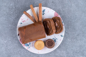 Chocolate roll cake, biscuits and cinnamon sticks on colorful plate