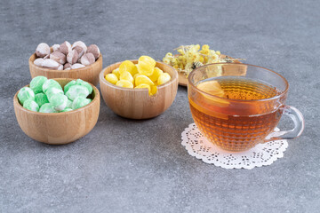 Bowls of colorful candies with hot tea on marble background