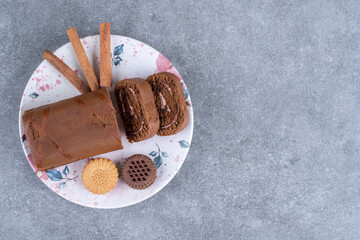 Chocolate roll cake, biscuits and cinnamon sticks on colorful plate