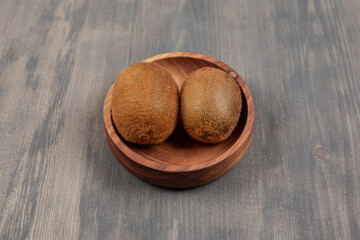 A wooden bowl with two fresh kiwis on a wooden table