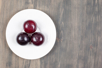 A white plate with three fresh plums on a wooden table
