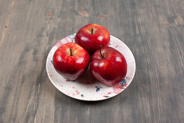 A white plate with red juicy apples on a wooden table