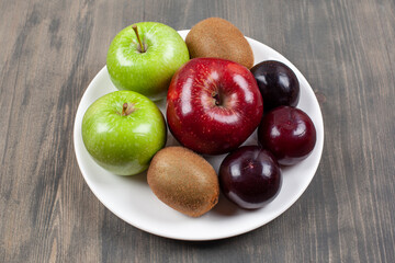 A white plate with juicy various fruits on a wooden table