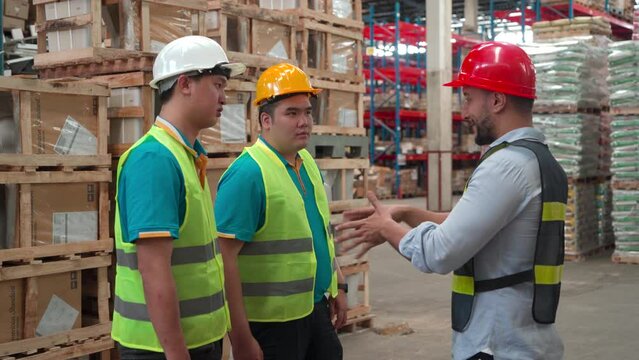 Two male employees standing listened to their boss explaining the work in the warehouse. caucasian man factory engineer teaching checking to colleagues. teamwork.
