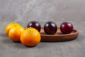 Tasty plums with delicious tangerines on a wooden plate