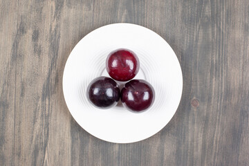 A white plate with three fresh plums on a wooden table
