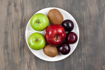 A white plate with juicy various fruits on a wooden table