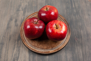 A brown plate with red juicy apples on a wooden table