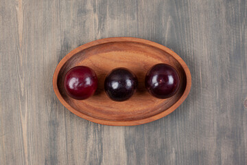 Three delicious plums on a wooden plate