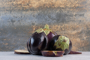 Fresh eggplants with water drops on stone surface