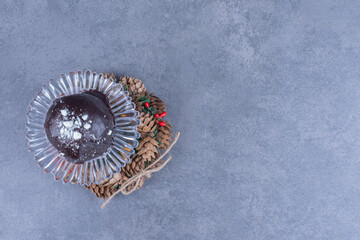 A glass plate with a chocolate cake and pinecones