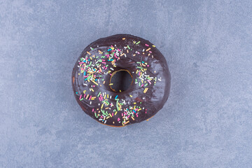 A chocolate donut with sprinkles on a gray background