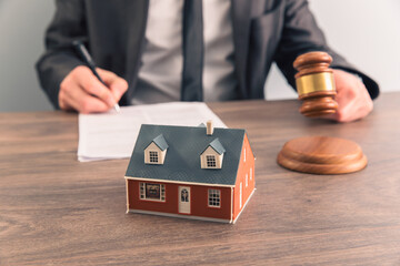 The hand of a judge with a gavel and a model of a house mediating property disputes in court