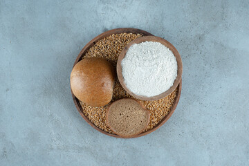 Rye bun with bowl of flour on wooden plate