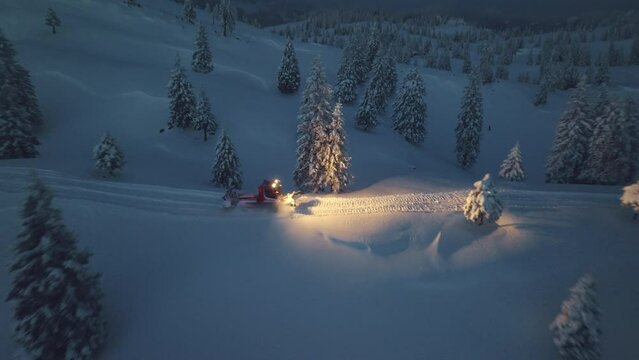 Aerial view of Snowcat ratrack with snowplow preparing the road in a dark. Driving through the deep snow piste in the ski resort. Heavy machinery mountain equipment.