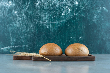 Two fresh buns on wooden board with wheat