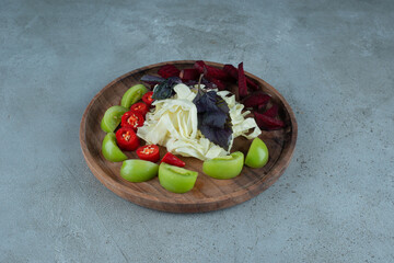 Slices of green tomato and chopped cabbage on wooden plate