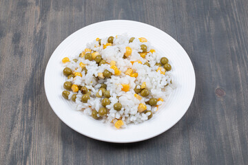 Rice with canned corns and peas on white plate