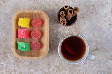 Cup of tea, cinnamon sticks and marmalade candies on marble surface