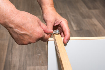 A man repairs furniture and screws a wooden rail with a bolt with a nut