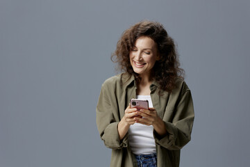 Happy cheerful smiling curly beautiful woman in casual khaki green shirt chatting with boyfriend using phone posing isolated on over gray blue background. Social Media Influencer concept. Copy space