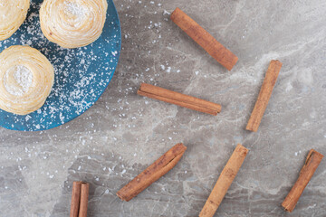 Bundle of cinnamon sticks next to flaky cookies on a board on marble background