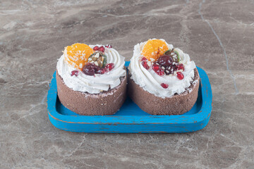 Small cakes with cream topping on a blue platter on marble background