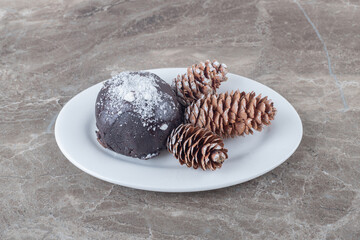 Vanilla powder and chocolate coated cake and three pine cones on a platter on marble background