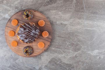 Marmelades, small donuts and a chocolate coated cake on a wooden board on marble background