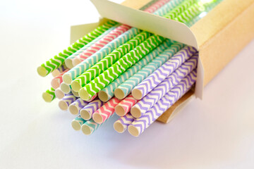 Closeup of colorful paper straws in brown cardboard packaging on a white background. Image with selective focus