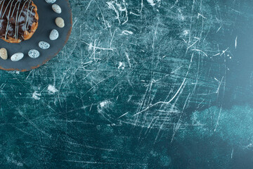 Candy rocks encircling a chocolate-topped cake on a board on blue background