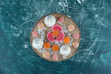 Vanilla-coated cakes and marmelades bundled on a wooden board on blue background