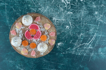 Marmelades and vanilla-coated cakes bundled on a wooden board on blue background