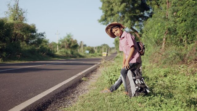 Teenager indian kid waiting for bus or taxi on highway road during holiday trip - concept of traveling, weekend holidays and liesure lifestyle.