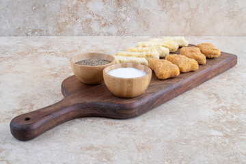 Chicken nuggets and cheese sticks on a wooden board with variety of sauces around