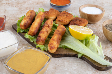 Fried chicken nuggets and grilled sausage sticks on a piece of lettuce with sauces around